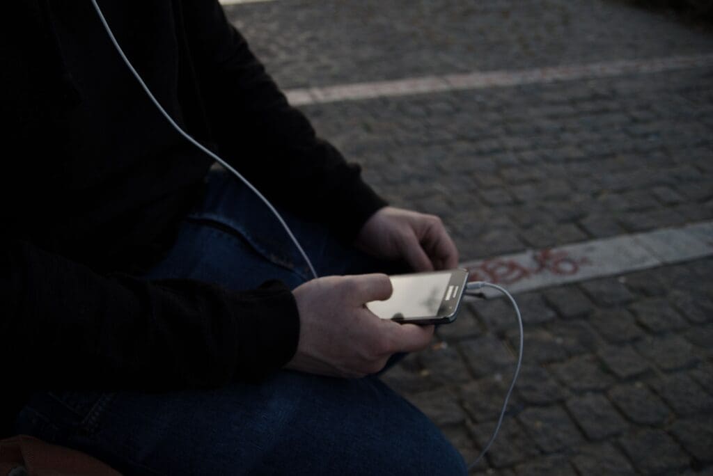 Person using a smartphone outdoors on a cobblestone street.