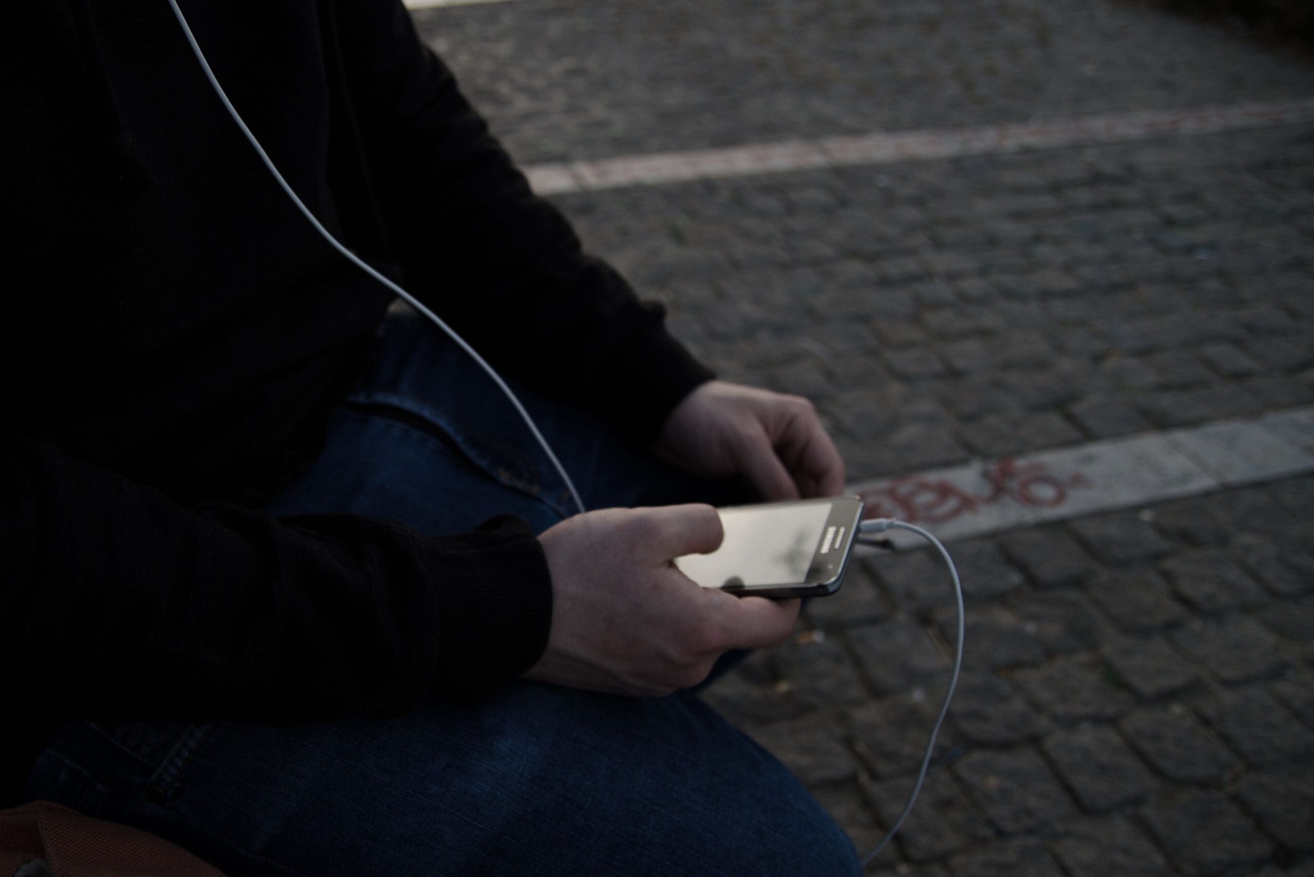 Person using a smartphone outdoors on a cobblestone street.